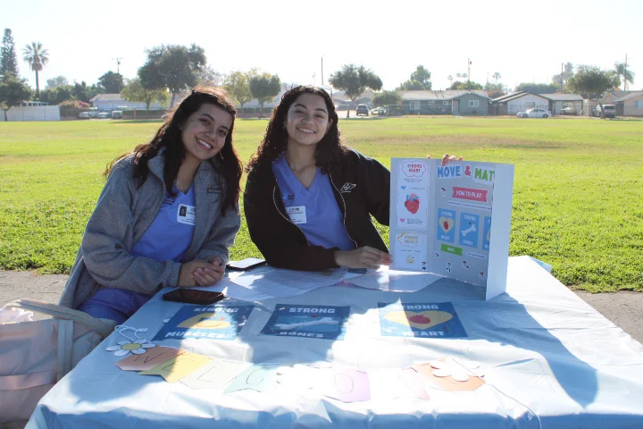Nursing students in blue scrubs at the Move & munch event holding informational signage.