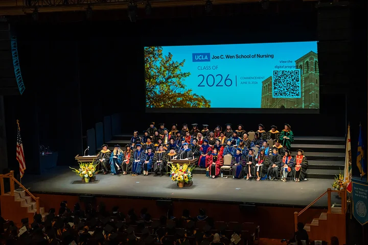 A wide shot showing the UCLA Nursing commencement stage with faculty seated in their cap and gowns. 