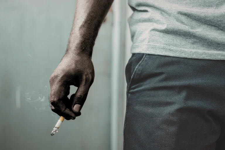 Close-up of a person’s hand holding a lit cigarette.