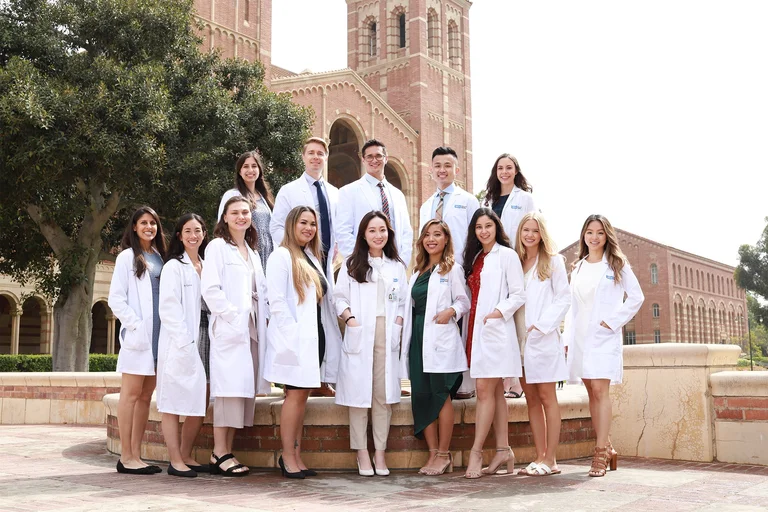 A group of nursing students wearing white coats and standing in front of the Royce Hall towers.