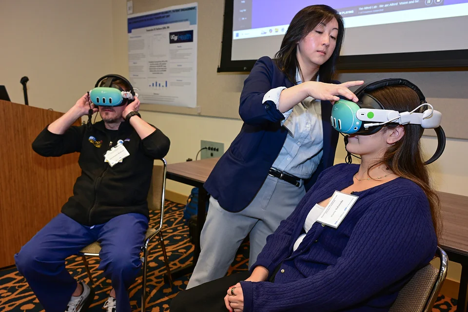2 conference attendees wearing VR headsets and being helped by a demonstrator during an interactive exhibit at the conference.