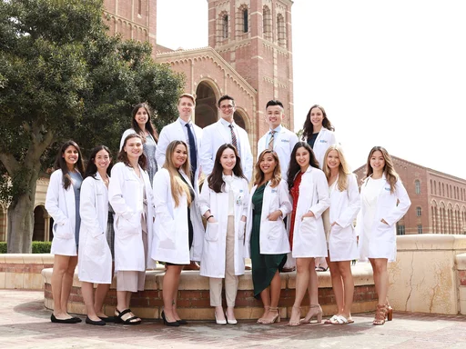 A group of nursing students wearing white coats and standing in front of the Royce Hall towers.