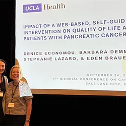 Eden Brauer and Denice Economou standing in front of a display screen at a recent conference presentation.