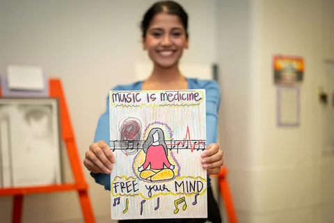A student holding up their art project, a painting with the words "music is medicine"