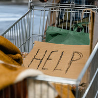 A photograph of a homeless person's shopping cart with a sign saying Help